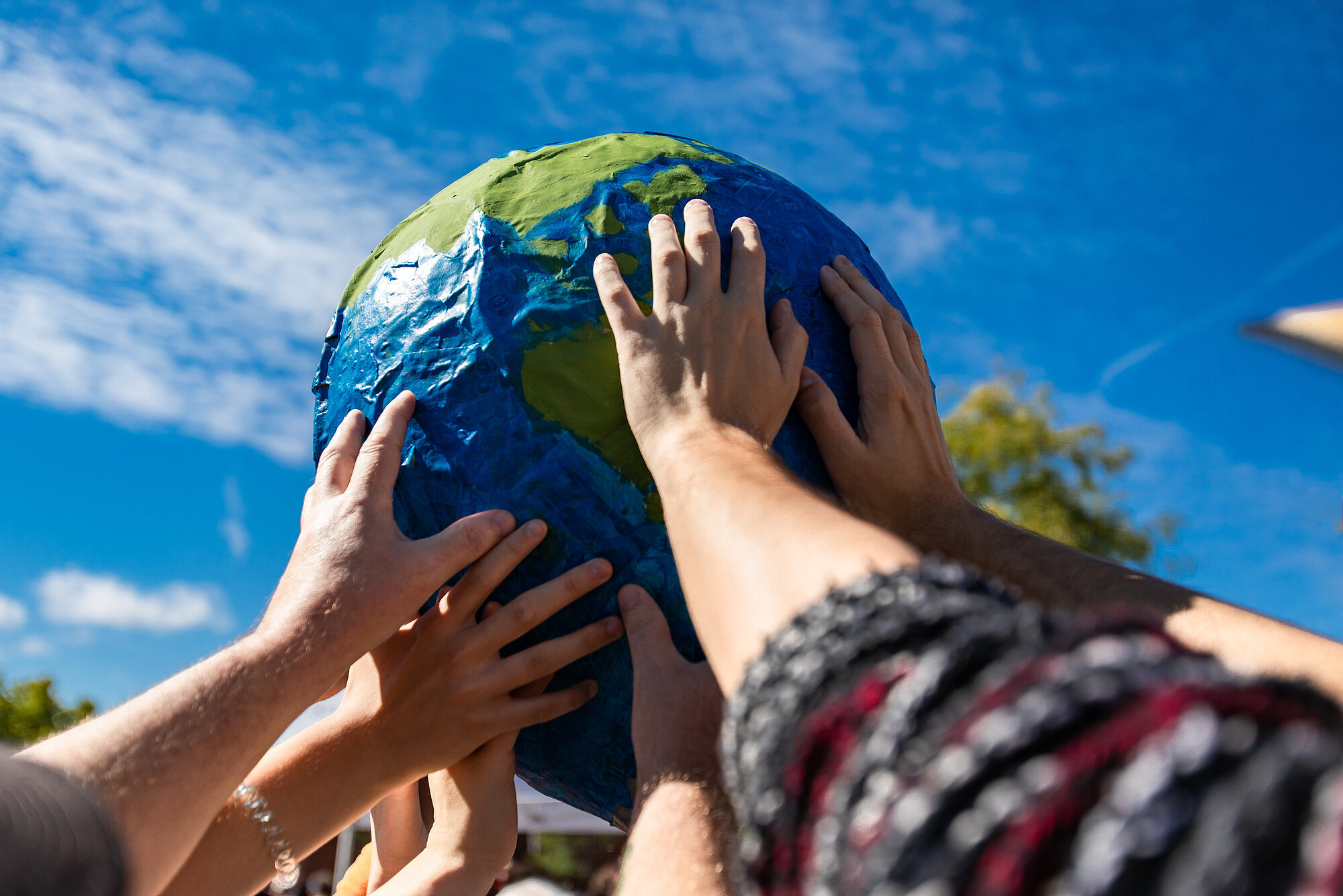 Many hands holding a giant terrestrial globe