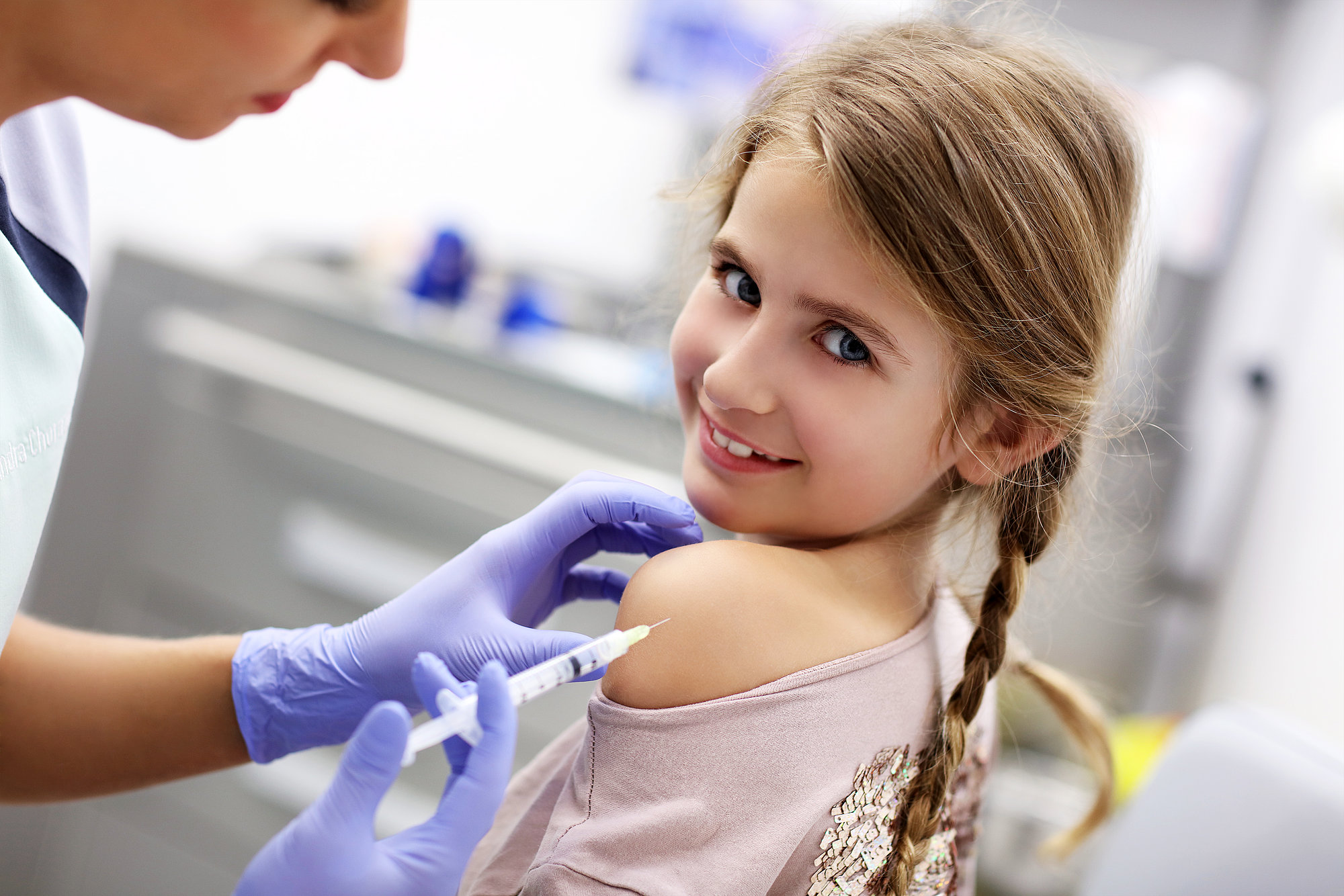 Startbild der Seite Impfaktionen und Impfaufrufe: Ein kleines Mädchen erhält eine Impfung in den Oberarm und lächelt dabei in die Kamera