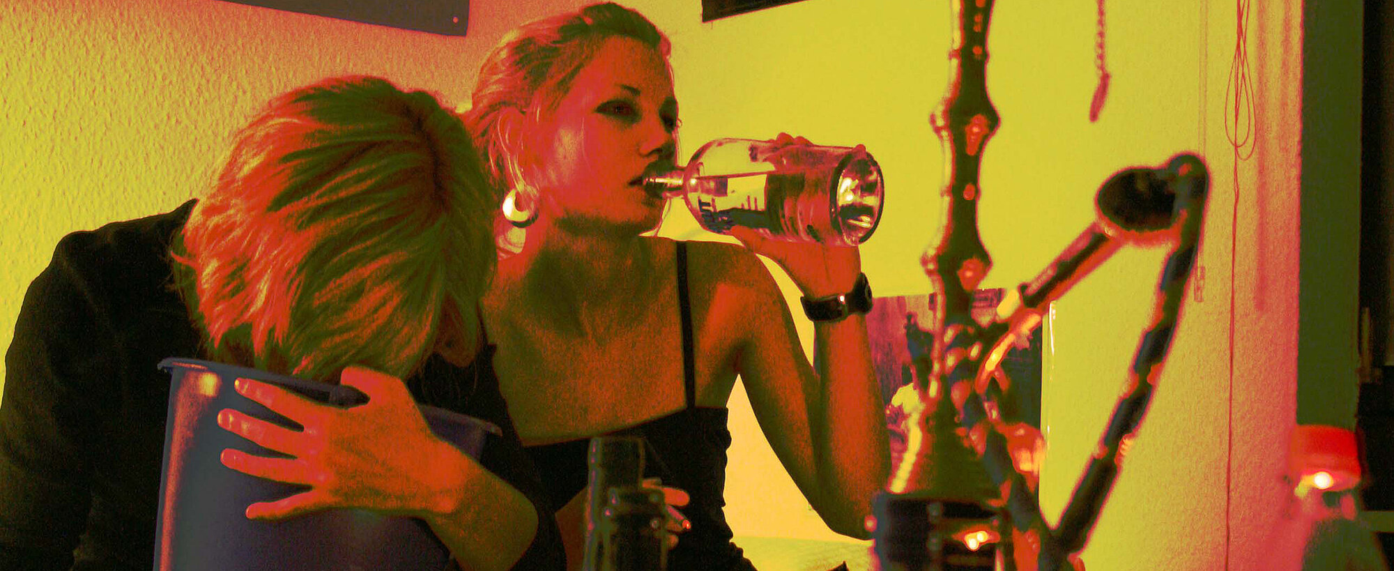 Startbild: Foto vom Alkoholpräventionsprojekt "Hackedicht - Besser geht's dir ohne!": Ein Mädchen trinkt Alkohol, ein zweites Mädchen erbricht sich in einen Putzeimer