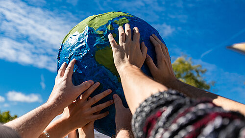 Many hands holding a giant terrestrial globe