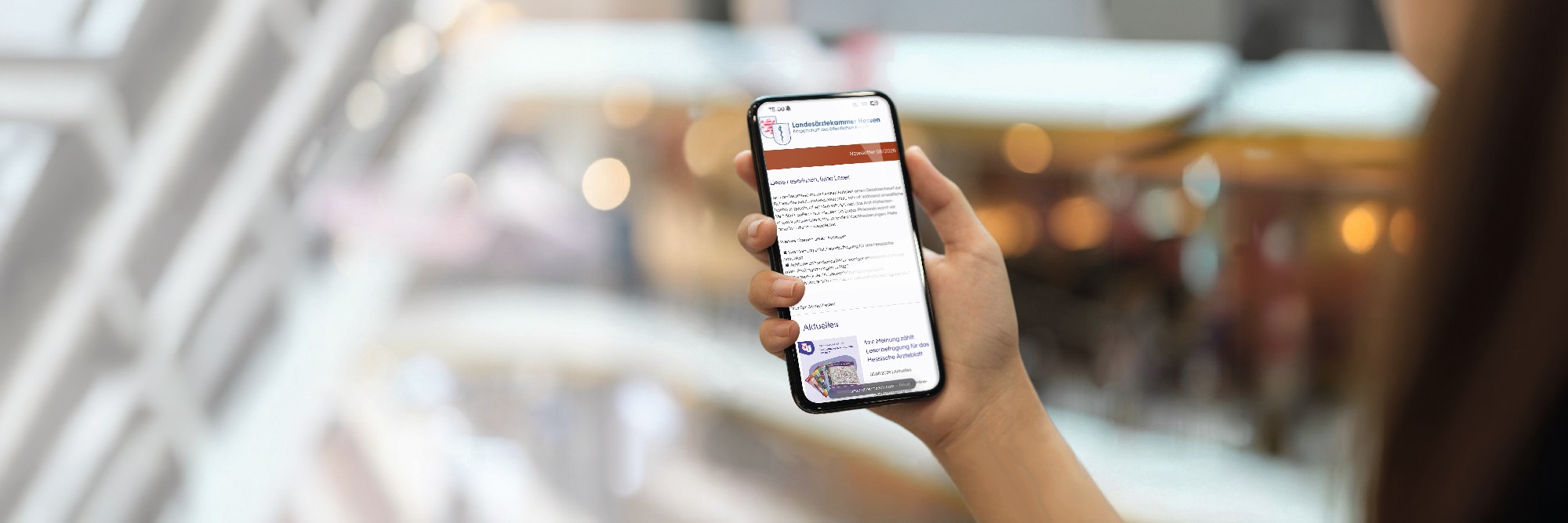 Eine Frau hält ein Smartphone in der Hand, auf dem der Newsletter der Landesärztekammer Hessen zu sehen ist.