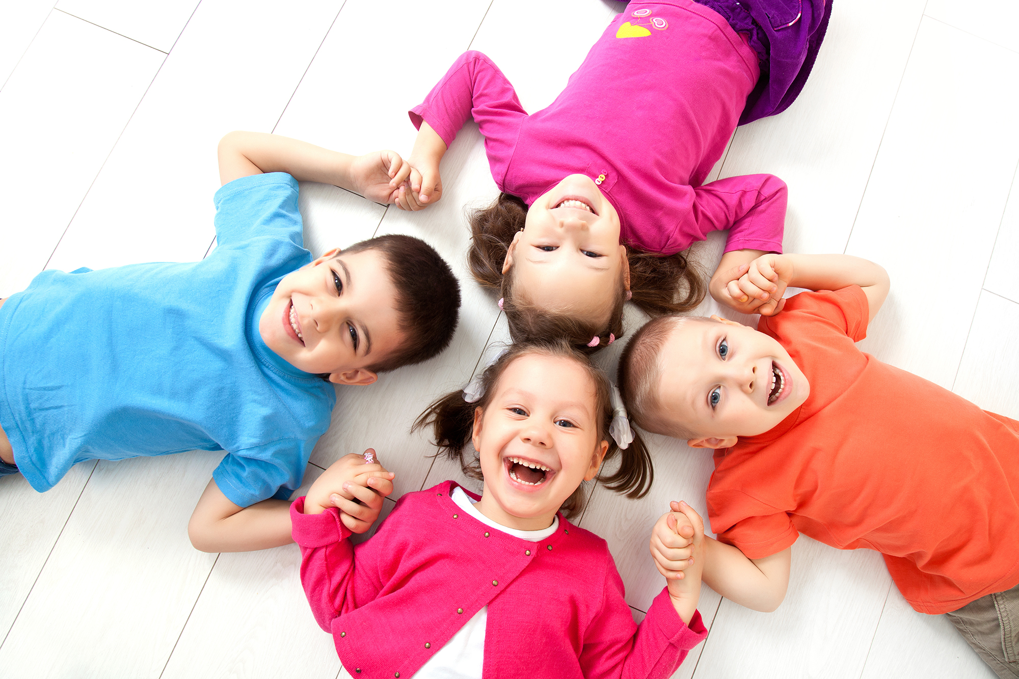 Startbild: Foto von fröhlichen Kindern, die im Kreis auf dem Boden liegen und sich an den Händen fassen